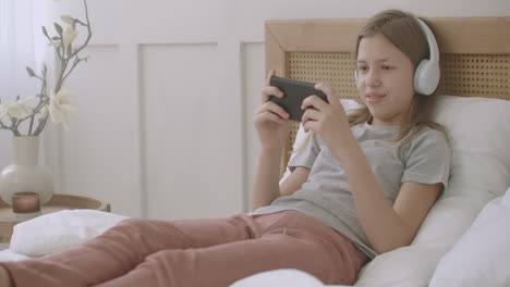 preteen-girl-is-playing-game-in-mobile-phone-lying-on-bed-in-home-after-school-classes-children-with-pathological-internet-use